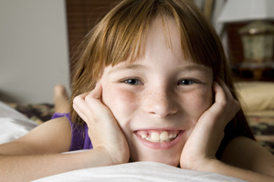 A girl smiles on a bed indoors.